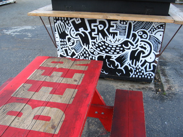 Picnic table in the Quartyard reads beer, next to a planter with fun artwork.