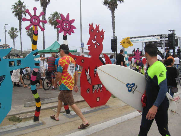 Some surfers pass fun public art on Newport Avenue. They hear music coming from the main stage by the beach.