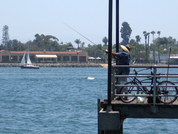Fisherman on pier and a sailboat.