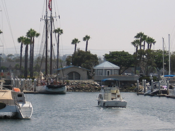 A boater heads into the dock, toward the tall ship Bill of Rights.