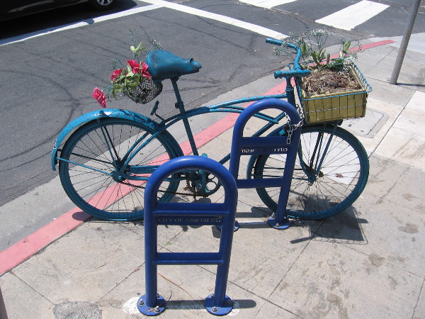 Someone's artistic bicycle has a potted plant in its basket.