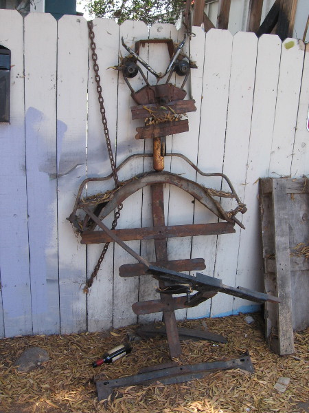 This rusty metal sculpture leans like a lazy old fellow against the white fence.