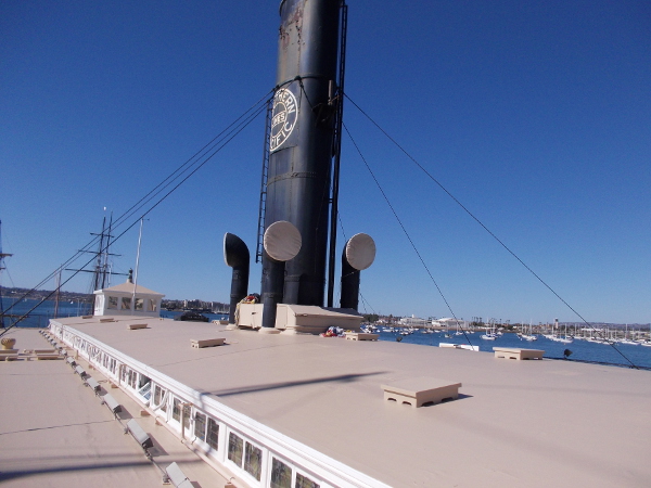 Photo over the roof of the ferryboat, with a black funnel projecting into the blue San Diego sky.