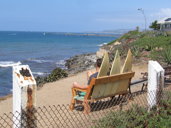 Sitting on a unique surfboard bench, gazing across the blue ocean.