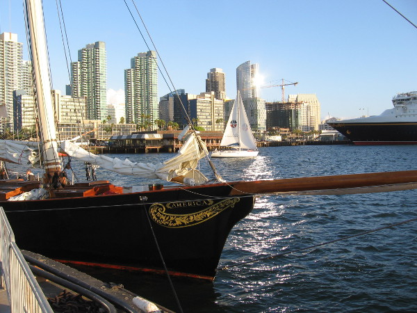 A sailboat glides between beautiful yacht America docked at the Maritime Museum of San Diego and the shining downtown skyline.