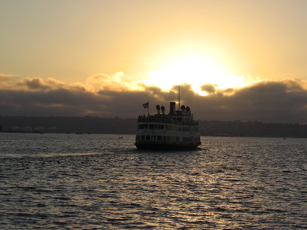 The darkening ship moves across the water toward a golden sunset.