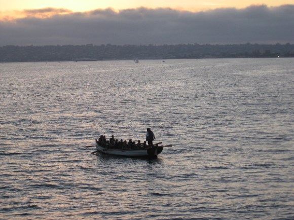 Youth row a Maritime Museum longboat as the sun sets, perhaps dreaming of finding pirate gold.