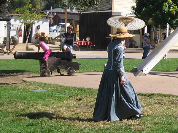 Lady with old-fashioned parasol walks through Old Town San Diego State Historic Park's Plaza de las Armas.