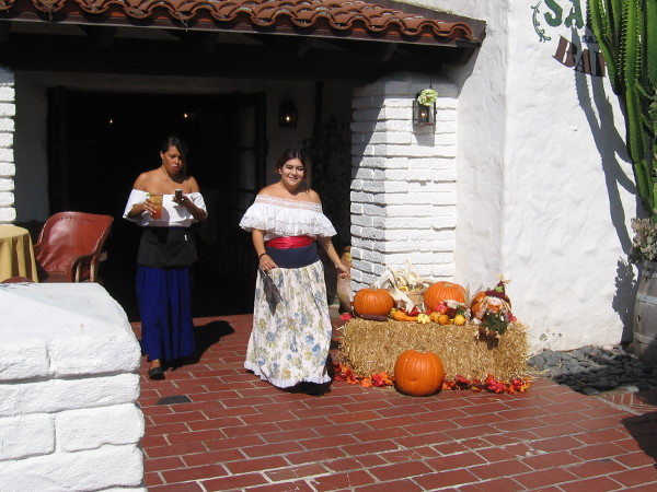 A smiling señorita walks near some pumpkins.