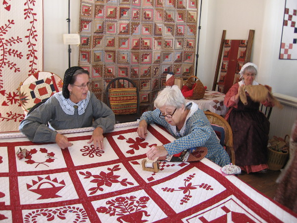 Ladies work on a quilt inside the Threads of the Past Living History Activity Center.