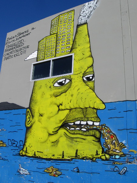 The yellow human head, topped by city buildings and a smokestack, vomits disgusting trash into the blue ocean.
