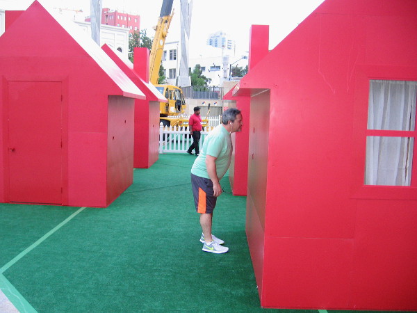 Someone in downtown San Diego peers through a spy hole into a tiny red house in Horton Plaza Park.