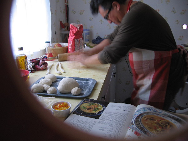 Inside one tiny house I see an actor in a small kitchen baking bread!