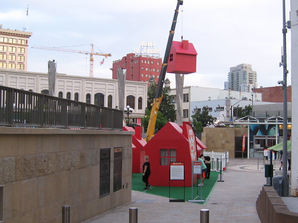 Several plain red houses stand in Horton Plaza Park--and one is dangling high in the sky from a crane!
