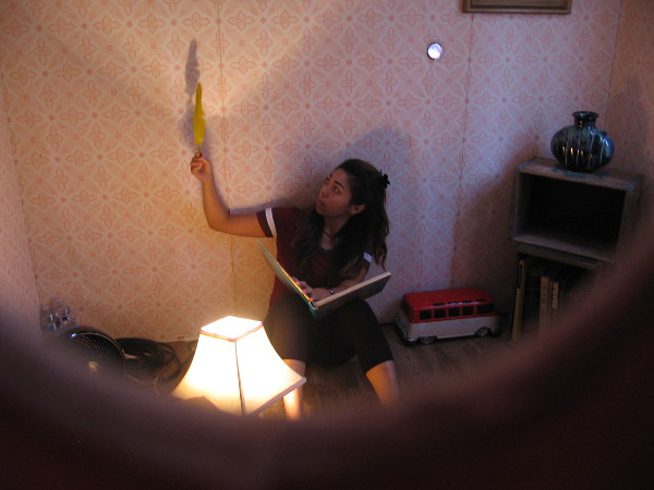 And inside this Model Home an actress is studying a feather, holding it up and turning it in the light. She seems to be quietly thinking.