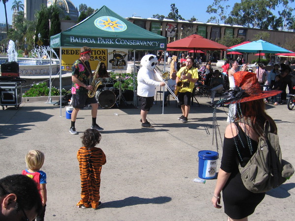 A panda and his pals were providing music in the Plaza de Panama. People in Halloween costumes look on.