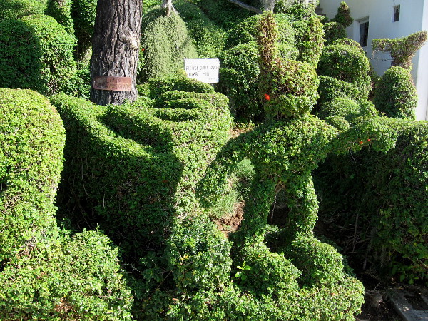 A funny rabbit stands and points among many topiary creatures.