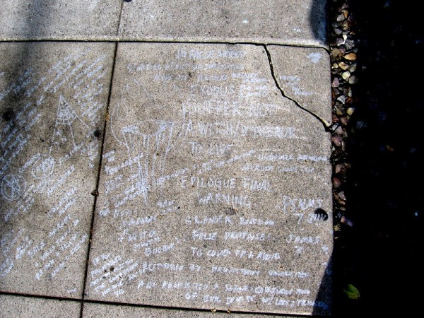It appears someone scratched many warnings, symbols, theories and ideas on a section of the sidewalk.