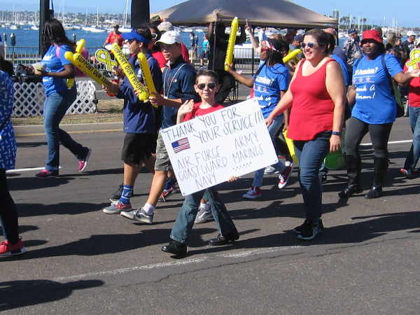 Kid holds a sign that reads Thank You For Your Service!!! Air Force - Army - Coast Guard - Marines - Navy