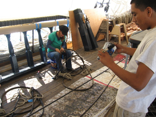 Museum volunteers work aboard HMS Surprise on a pleasant Sunday. Cables from the ship's rigging are readied, as a section of new deck is caulked.