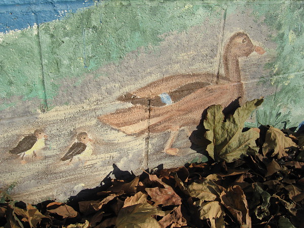 A mother duck and two ducklings walk among leaves on the Our River mural in Mission Valley.
