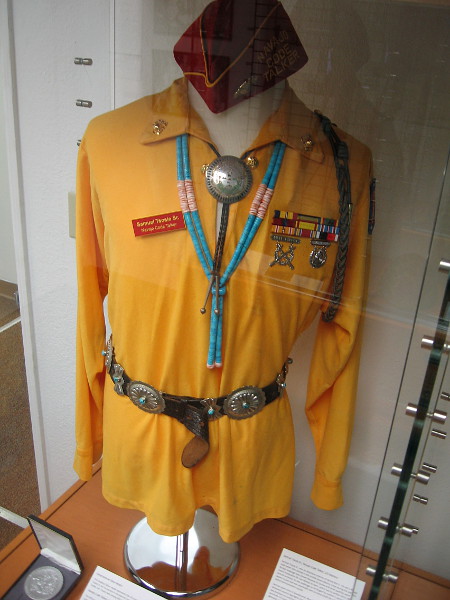 Official uniform of the Navajo Code Talkers includes a red cap, Navajo jewelry, gold shirt, patch on upper arm, light-colored trousers and abalone-colored shoes.