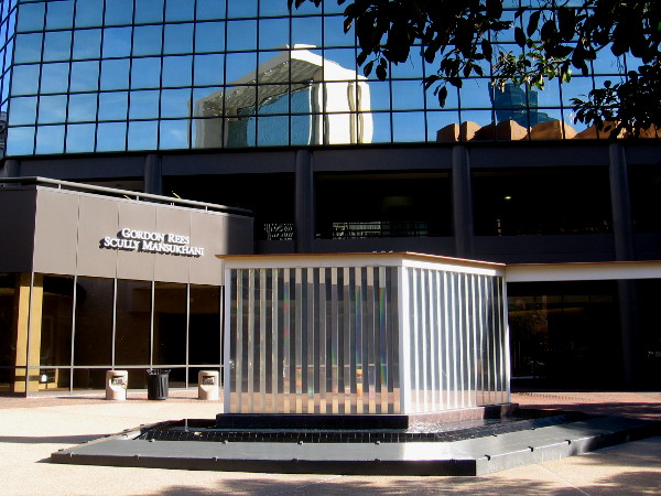 A cool prism wall sculpture, beneath reflections of nearby downtown buildings.