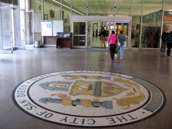 People walk toward the San Diego City Information Center past a large terrazzo Official City of San Diego Seal.