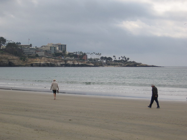 Two people walking south along the smooth beach. La Jolla Cove can be seen across La Jolla Bay.