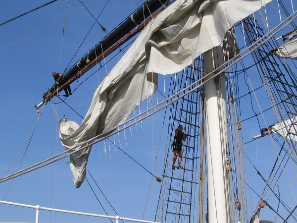 Crewmembers take to the ship's rigging to do some work.