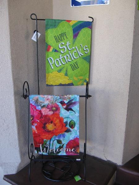 A green banner near the entrance to the Balboa Park Visitors Center anticipates St. Patrick's Day. A banner with bright flowers and a hummingbird anticipates the arrival of spring.