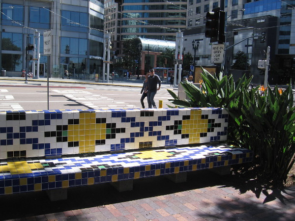 Gazing from the forecourt's plaza over a tiled bench toward America Plaza and buildings along Broadway.