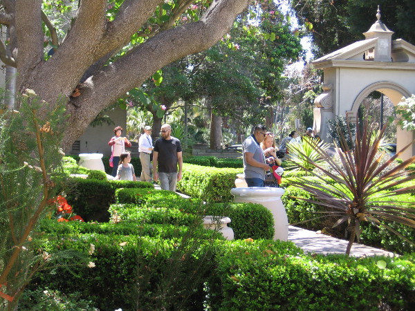 People walk through Balboa Park's sunlit Alcazar Garden on a beautiful spring Sunday.