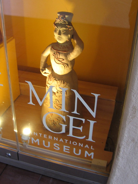 A clay female figure on display in one glass case outside the entrance to the Mingei International Museum.