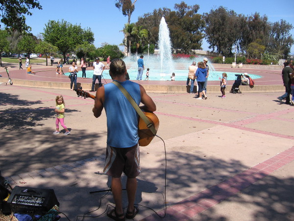 A guitarist plays in some shade near the splashing Bea Evenson Fountain in the Plaza de Balboa.