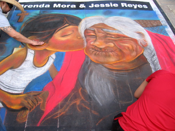 Young girl kisses a happy wrinkled woman. Touching chalk art by Brenda Mora and Jessie Reyes.