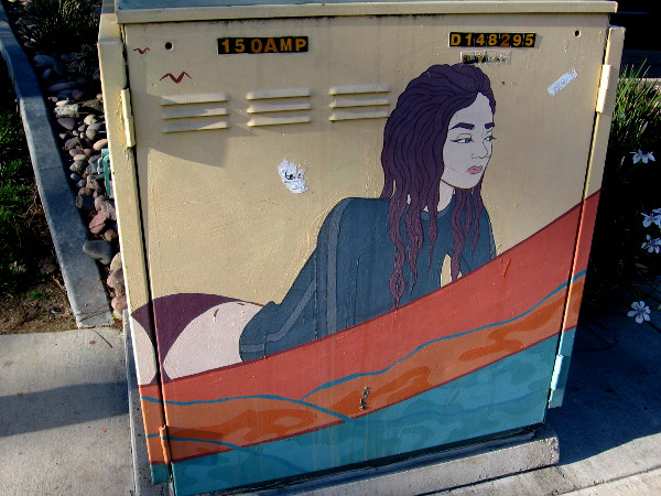 Surfer girl street art on another electrical box. She's on her surfboard awaiting a perfect wave.