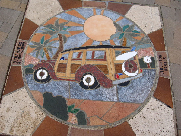 A woodie with surfboard under palm trees and a shining sun. This mosaic greets people walking down the sidewalk in Solana Beach.