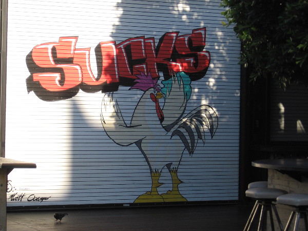 A street art chicken spray paints graffiti on a restaurant door.