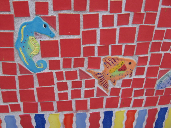 Small sea creatures made of ceramic swim about a tile mosaic bench at a bus station in Solana Beach.