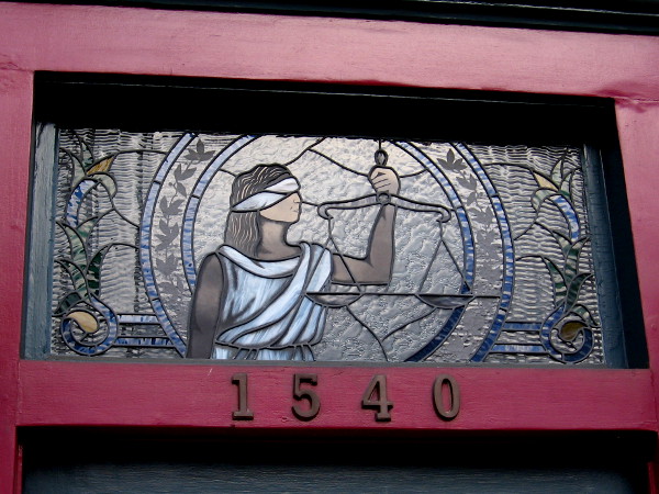 A beautiful window above the entrance of Sidiropoulos Law Firm on Sixth Avenue depicts blind Justice holding her scales.