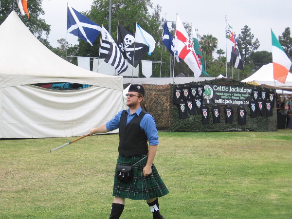 A Scottish drum major practices on the field, with flags flying in the background.