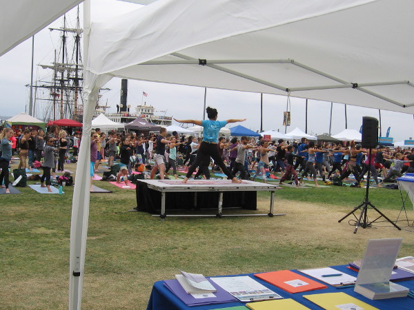 An energetic instructor poses on a platform, helping to lead the many yogis.