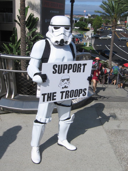 A Star Wars stormtropper holds a humorous sign. Support the Troops.