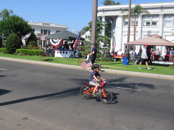 Kid heads down Orange Avenue on a small bicycle decorated for Independence Day.