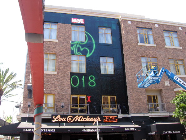 A Marvel building wrap is being applied above the Lou & Mickey's sign.