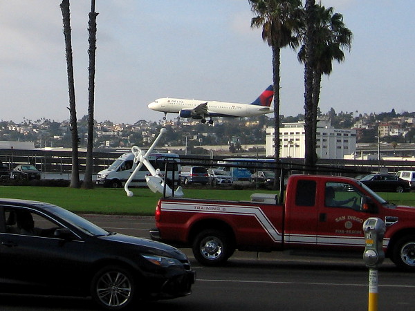 A plane lands at San Diego International Airport, just beyond a large white anchor at Harbor Drive and Laurel Street.