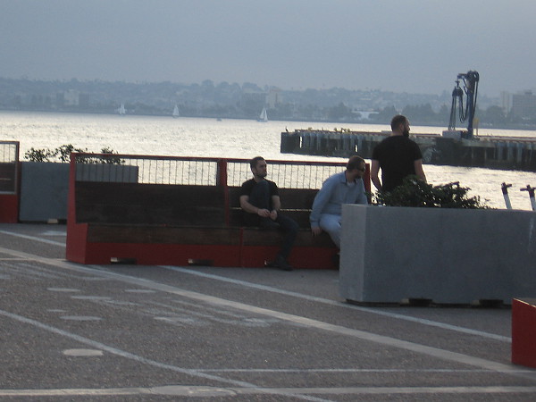 People relax on one of the benches along the edge of Broadway Pier. The fog-like marine layer is coming in over Point Loma as nightfall approaches.