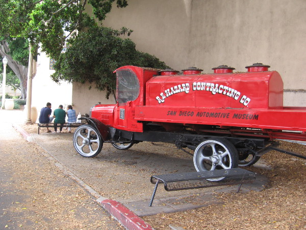 People relax on a bench by the old Mack Water Truck just outside the entrance of the San Diego Automotive Museum.