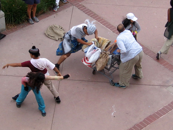 Performers tussle over the shopping cart, while a nearby couple dances.